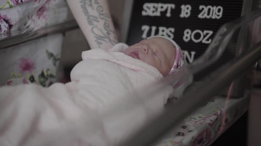 Tattooed woman puts the newborn infant on cradle in the daytime