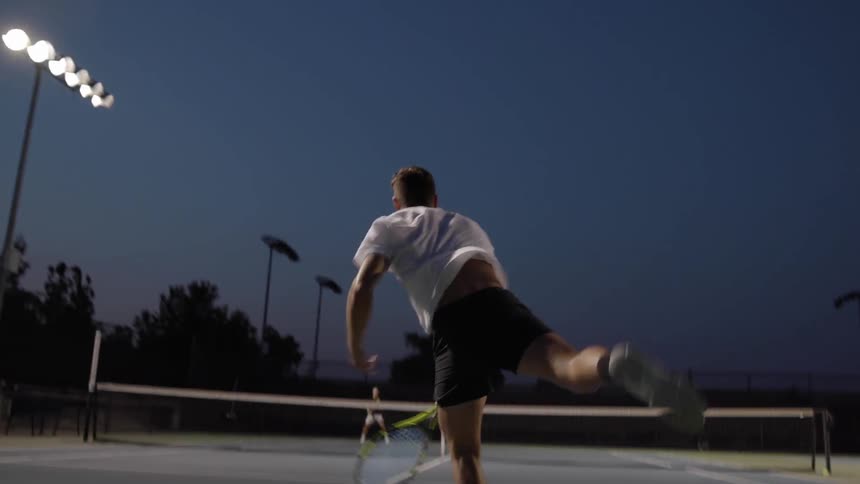 A man hitting a tennis ball outdoors at night