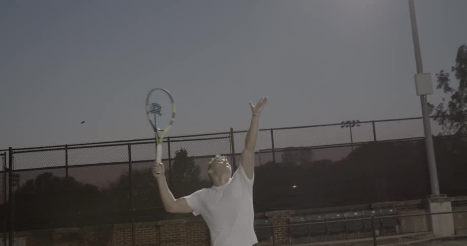 A man serves a tennis ball on a court at night