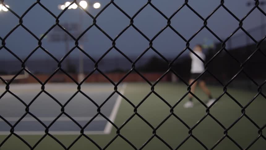 A tennis player returning the ball with a backhand volley on a tennis court during the night