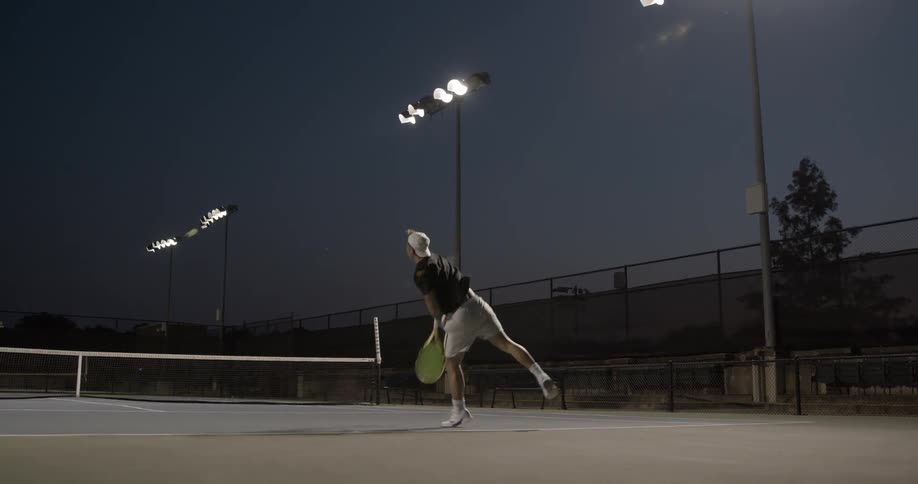 A man at night serving a tennis ball