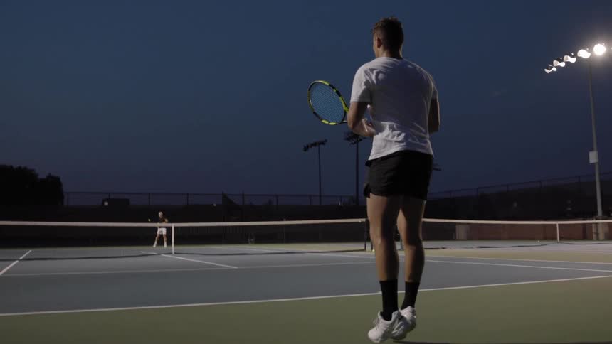 Two people are playing tennis on the tennis court at night