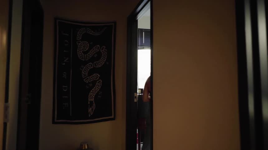 Woman walks down a hallway then turns to enter a bedroom and sit down at a desk