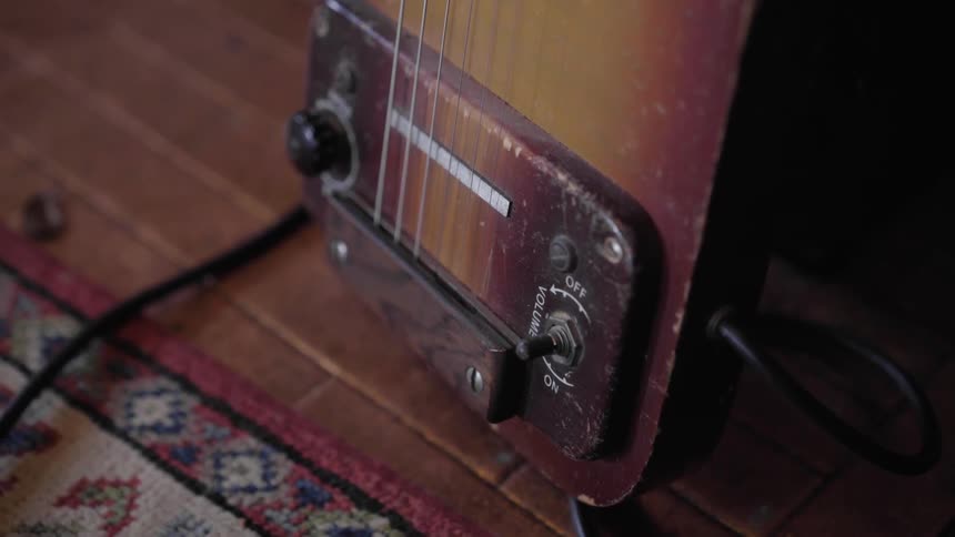 The strings and pickups of an old fashioned electric guitar are seen as the guitar rests a floor next to a rug