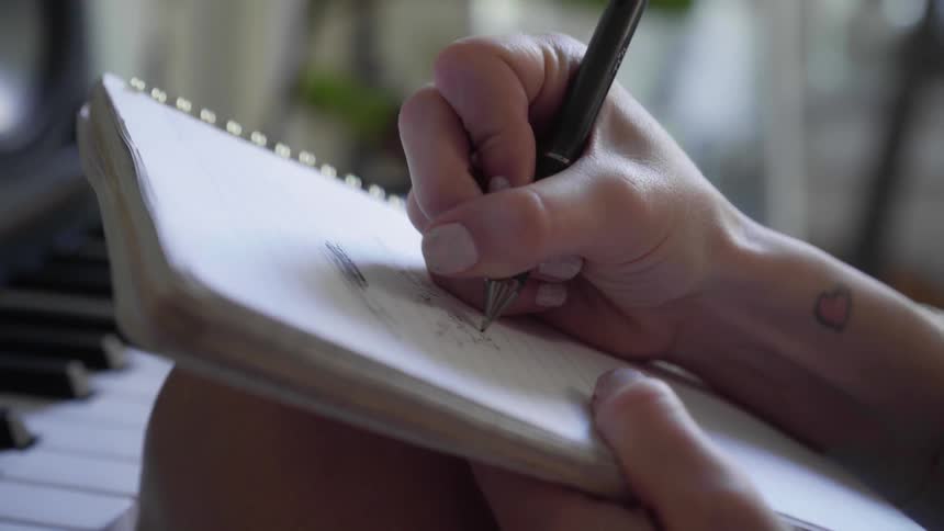 A woman in front of a piano writing on a notepad