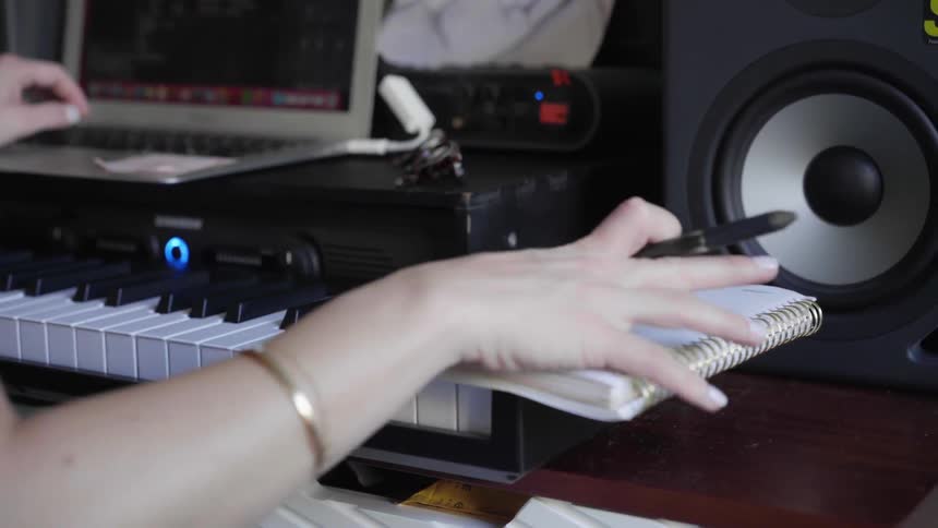A white woman types on a laptop computer and then writes in a notebook