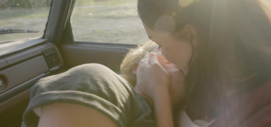 A woman plants kisses all over a young mans face while they sit in a car