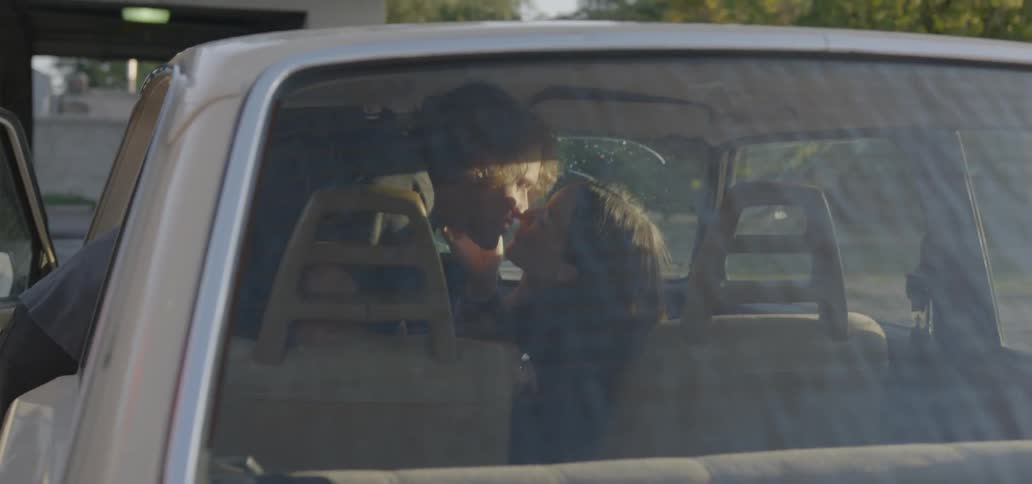 A couple exchange kisses inside a car