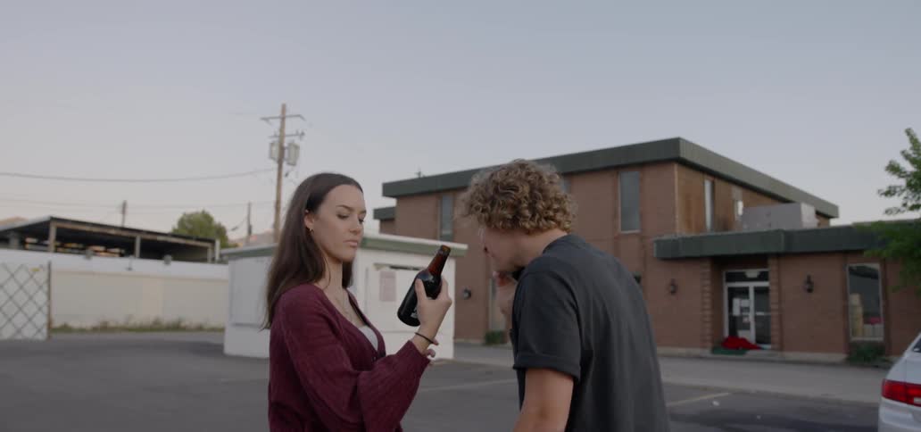 A man and woman sharing a beer in a parking lot