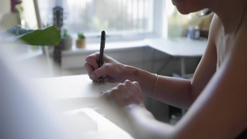 A white female is writing in a notebook that is placed on top of a keyboard