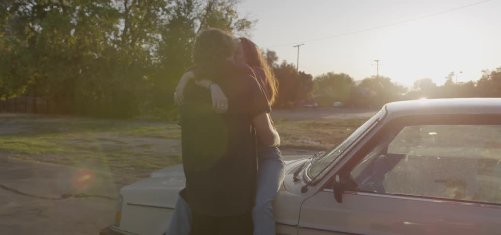 A young couple embrace on the boot of a car at sunset
