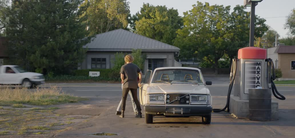 A man and a woman at a gas station walking towards a car and hugging