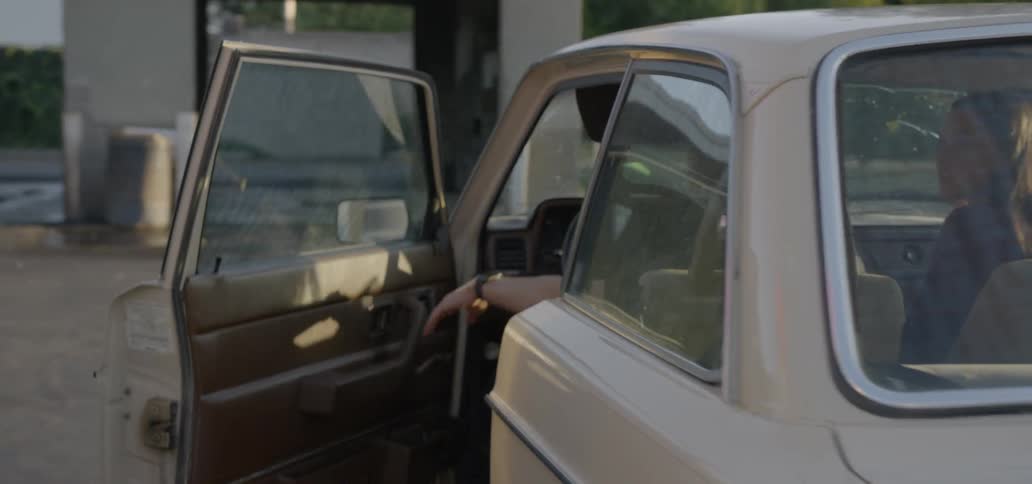 A young white man gets into a tan car and closes the door