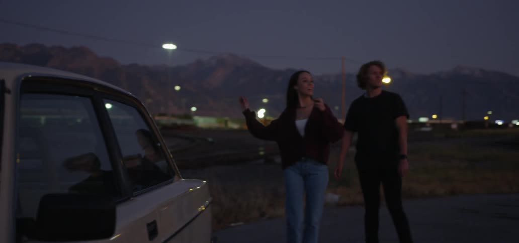 A man and woman throwing rocks near a field at night