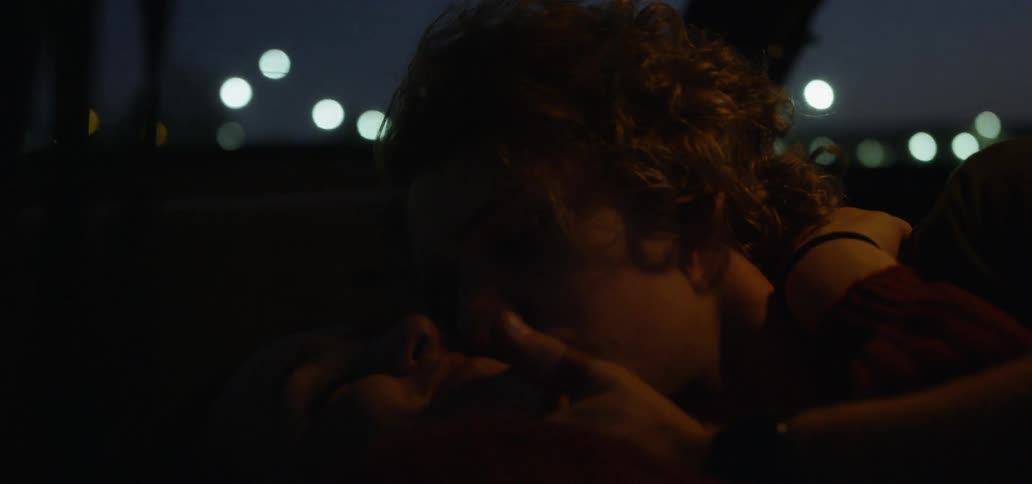 A young man kissing a young woman in a car at night