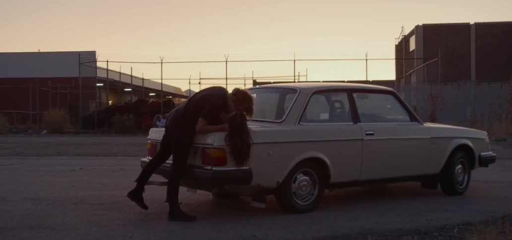 A woman laying on the trunk of a car making out with a man