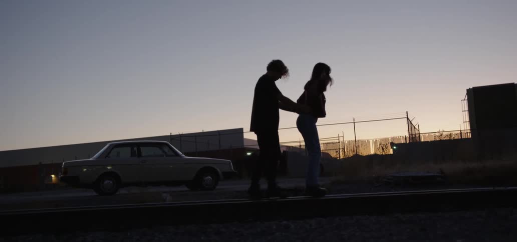 A young man and a young woman walk on a railroad track together