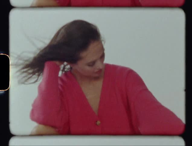 A woman in a pink sweater smiles and tosses her hair around in a strong breeze