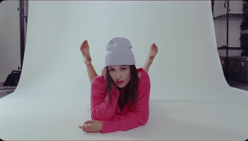 A woman with a hat and sweater laying down on a white backdrop