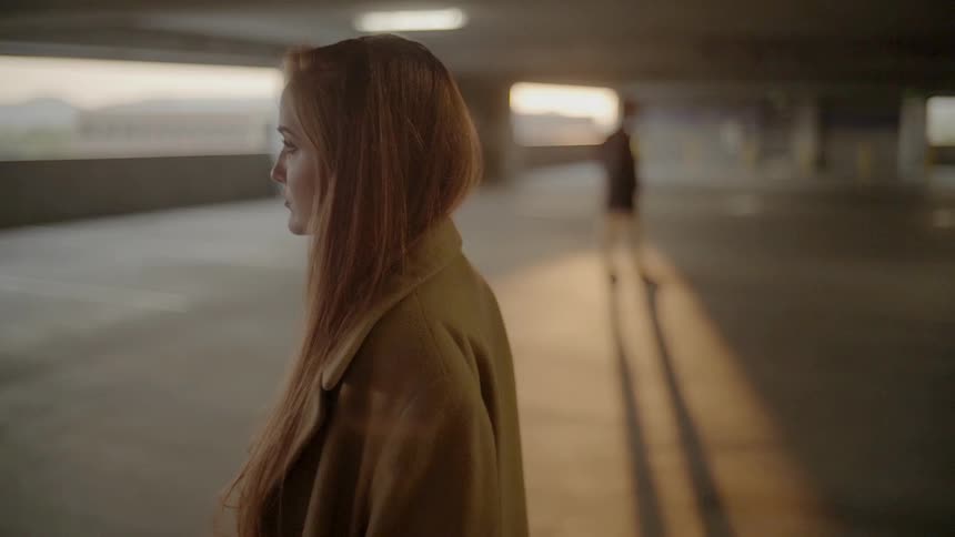 A woman an and out of focus individual posing in a parking garage