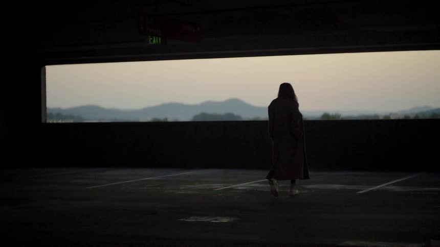 A woman wearing a long coat walks across a parking garage