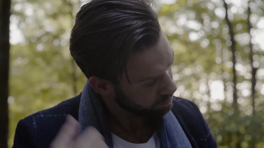 A man fixes his hair and jacket while standing in the woods