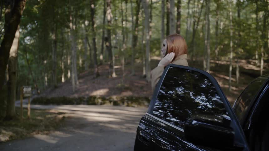 A white female gets out of the passenger side of a black sedan near a trail head at a park