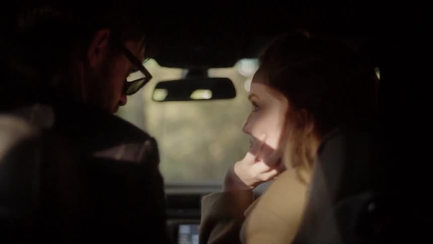 Two people talk in the front of a vehicle