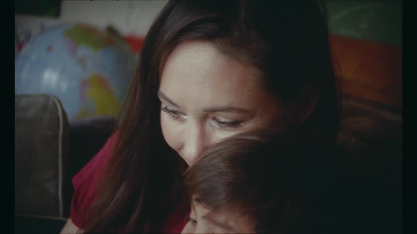 A boy sitting in his mom's lap and reading a book coughs and sniffles