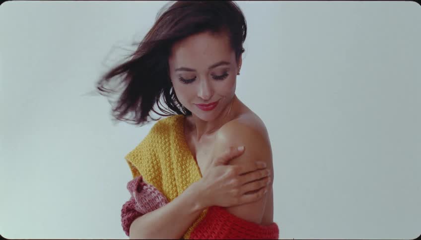 A woman caresses her bare shoulder while posing for a photo wearing a sweater