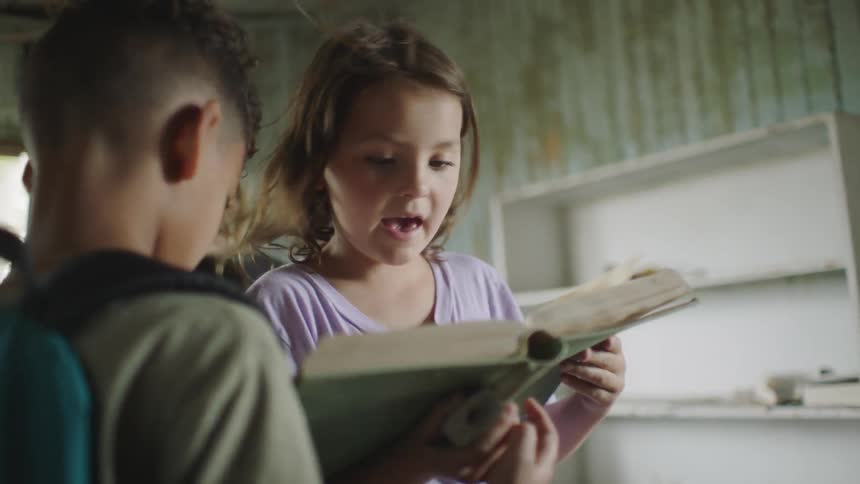A little girl and a little boy are looking at a book little boy has a backpack