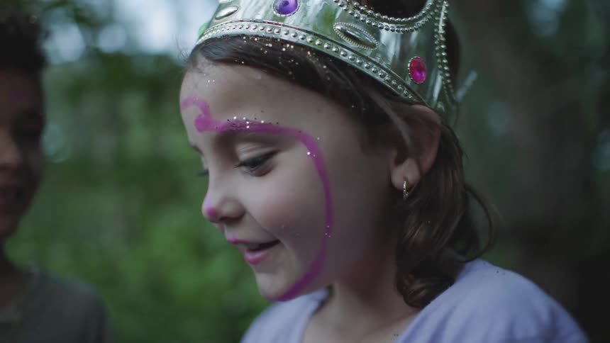 Little girl wearing a toy crown and a sparkling makeup smiles on camera