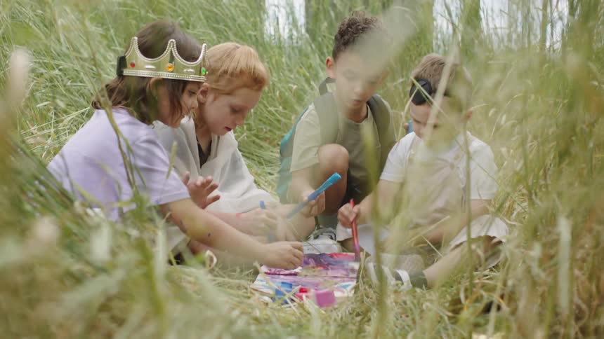 The children are sitting in the grass painting with markers