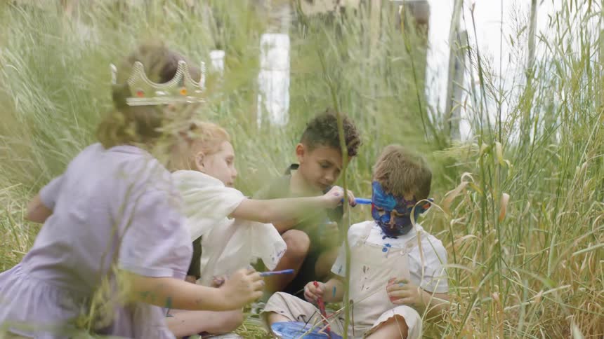Group of kids painting another kids face of blue in the middle of the tall grass