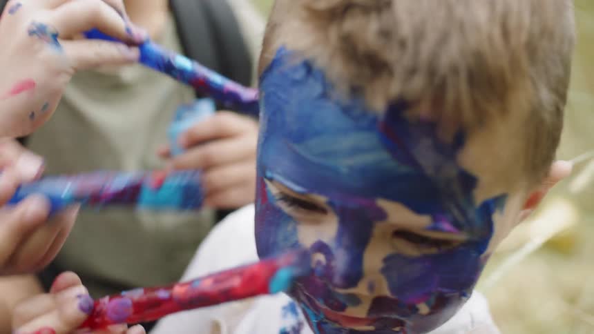 Group of kids painting the face of a toddler of blue