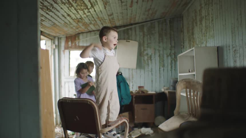A child standing on a chair with other children nearby playing