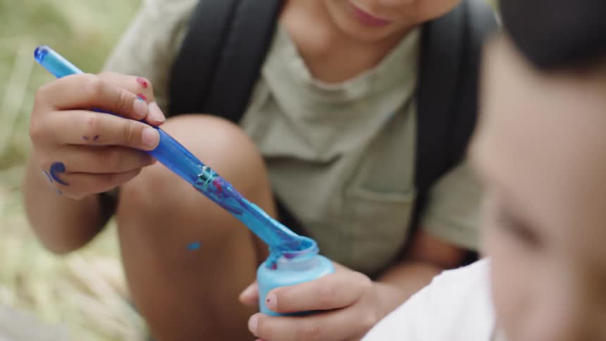 A young boy crouches and paints while talking to friends