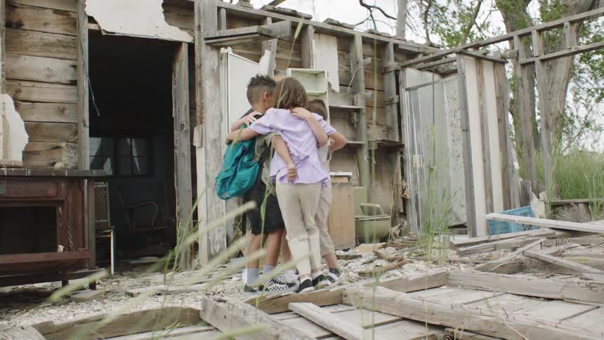 Four children dance in a circle together outside a wooden shack