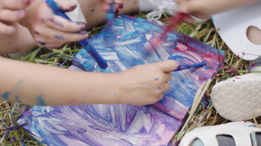 Children paint paper while sitting outdoors
