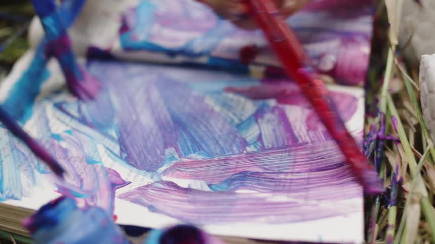 A person painting in a book using several paint brushes