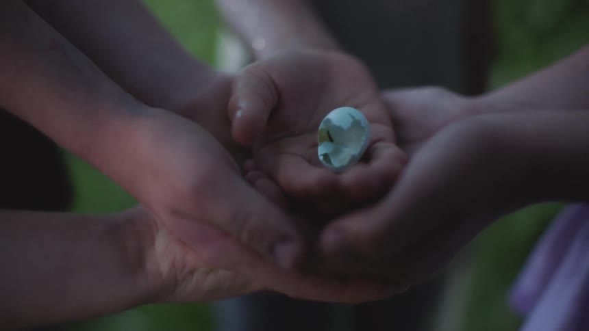 A boy with a eggshell in his hand while other boys placed their hands underneath his hand