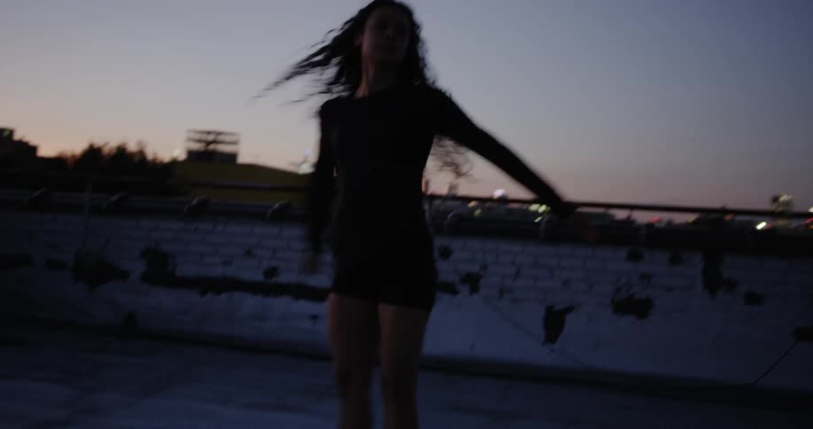 Woman dancing on the rooftop of building at sunset