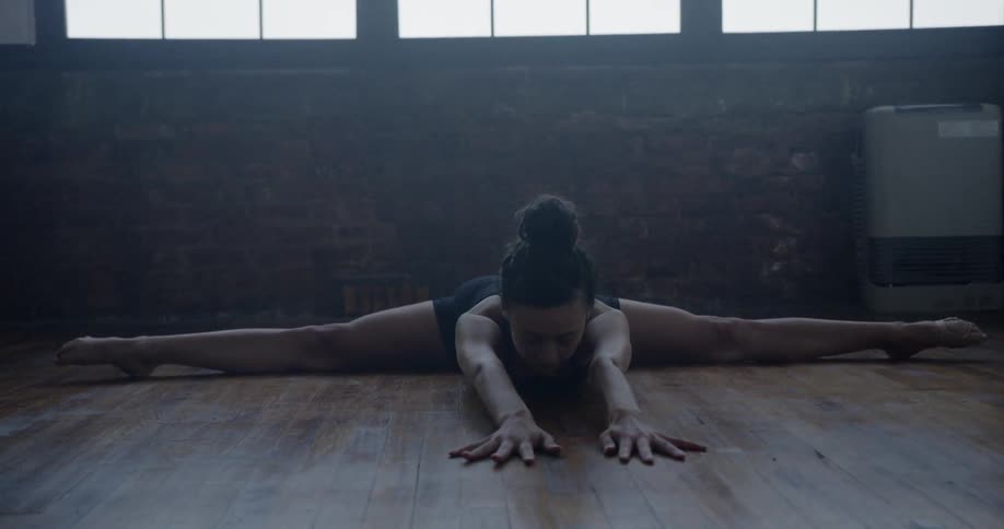 A young woman does the splits before raising her arms then leaning forward on the ground