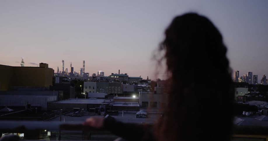 A young woman stands and looks out at the city