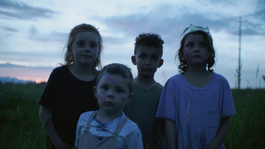 Dirty children standing in middle of a field at sunset
