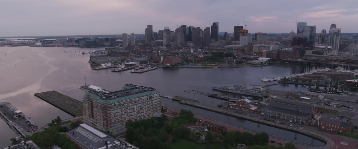 Cars travel on a highway heading towards a city on a harbor with docks and piers