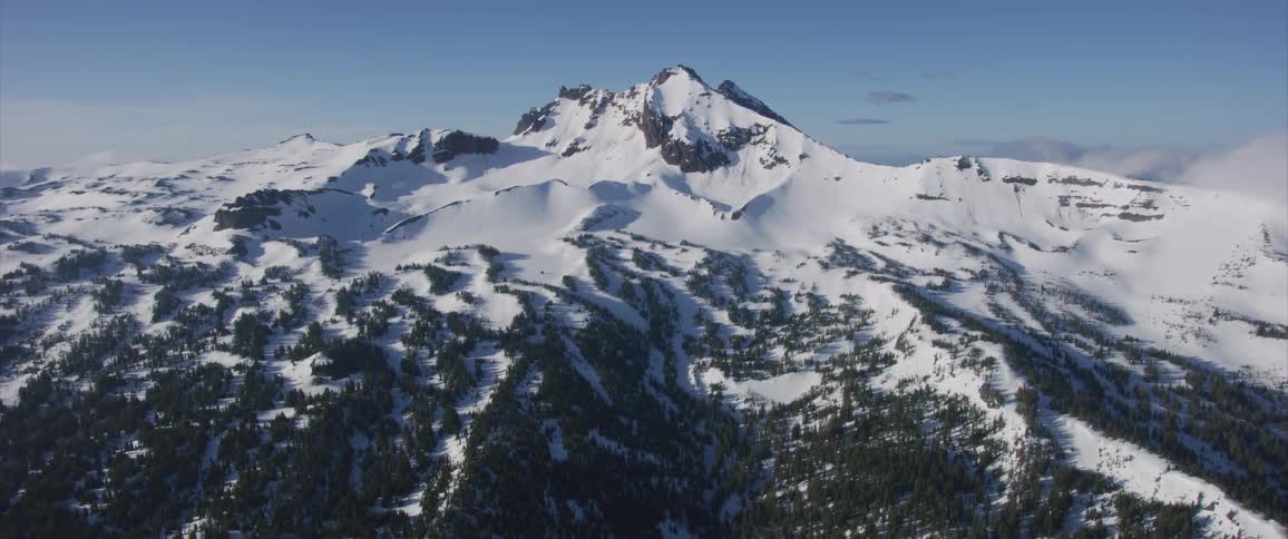 Trees and snow cover ridges leading up to a jagged peak