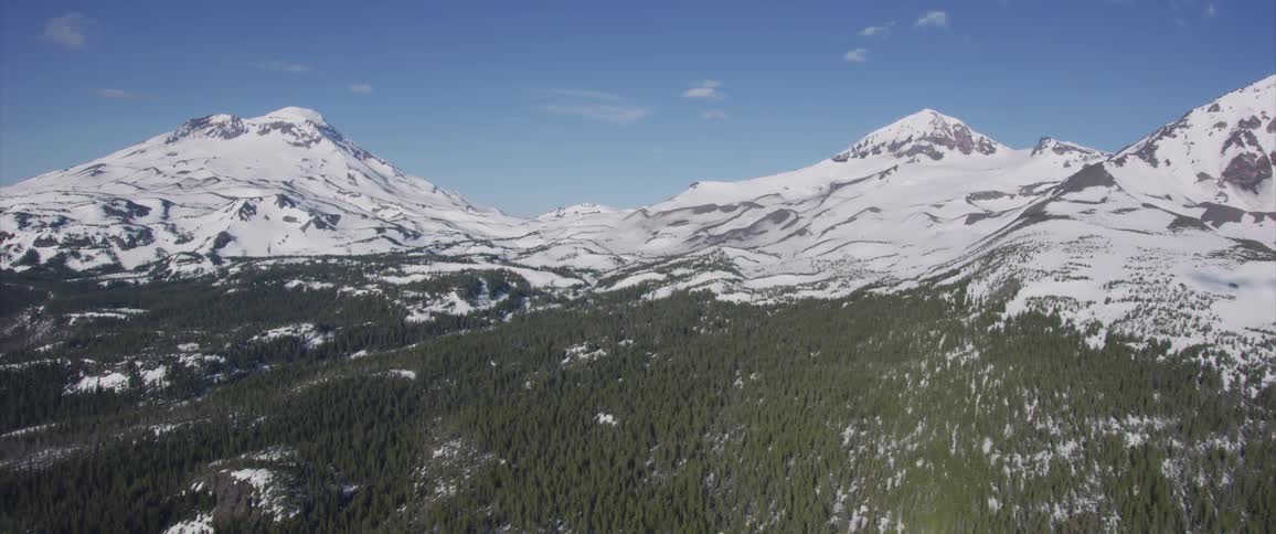 Camera flies along the snowy mountains covered by forest