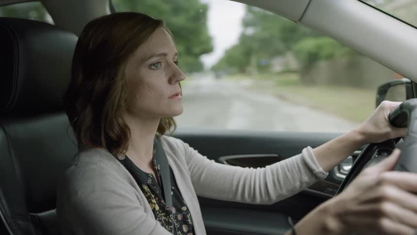 A petite white female drives a car with leather seats through a suburban area