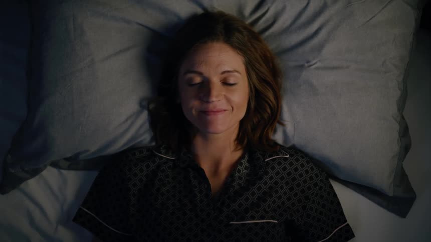 A woman in bed, closes her eyes with a restful expression to finally sleep.